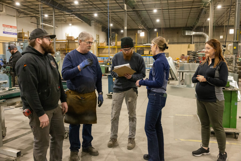 Four people discussing plans in a large industrial warehouse.